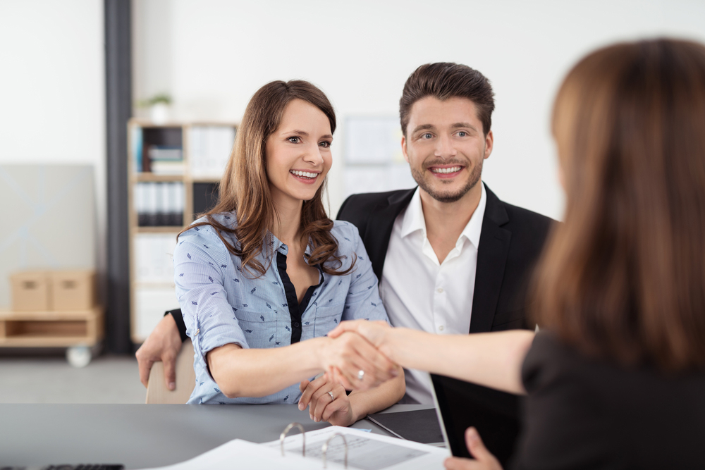 Happy Young Professional Couple Shaking Hands with a Real Estate Agent After Some Business Discussions Inside the Office.-2